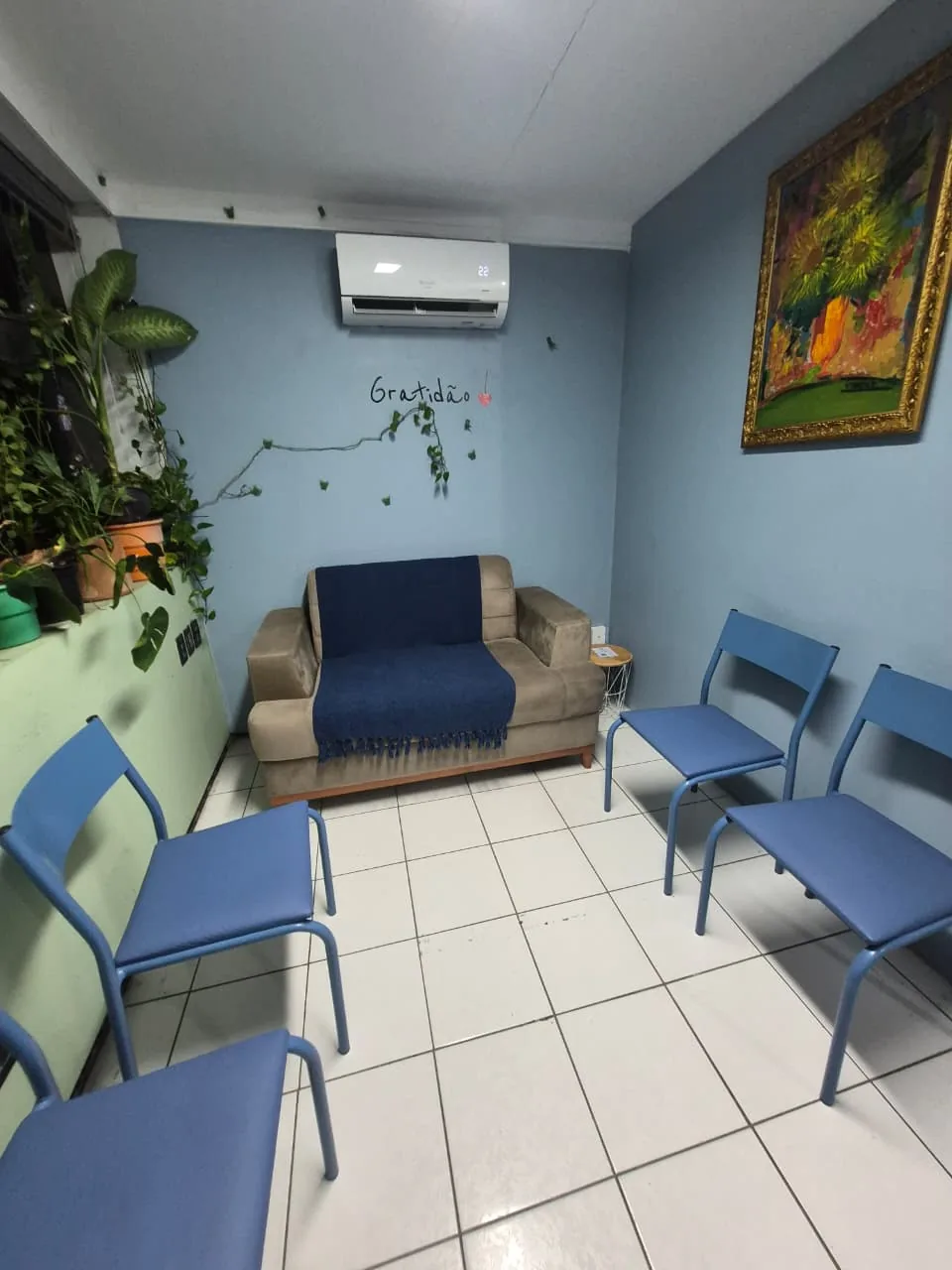 Sala de espera do consultório com sofá, plantas e a palavra Gratidão escrita na parede azul