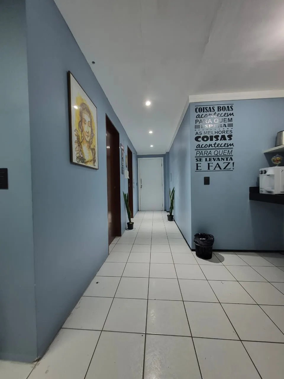 Corredor de acesso às salas de atendimento do consultório, com quadros nas paredes azuis