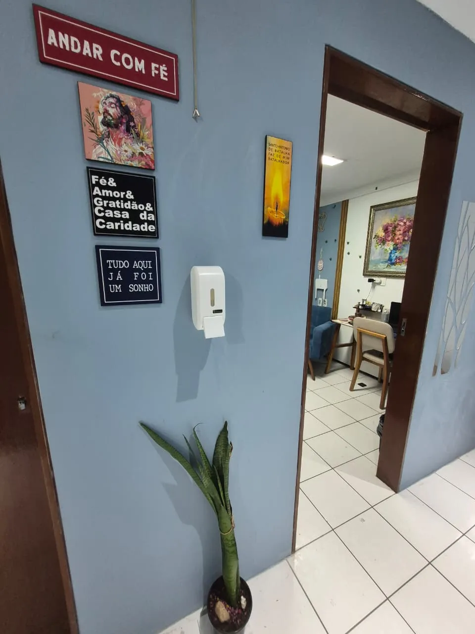 Entrada da sala de atendimento do Dr. Leonardo Alano, com quadros e plantas na parede azul